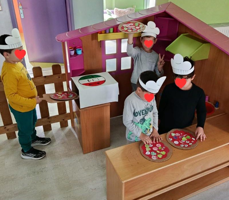 Παιδιά στο Τμήμα Προνηπίων παίζουν το παιχνίδι των ρόλων "μαγειρεύοντας" σε ξύλινη κουζινίτσα, αναπτύσσοντας τη φαντασία τους στην Καραμέλα.